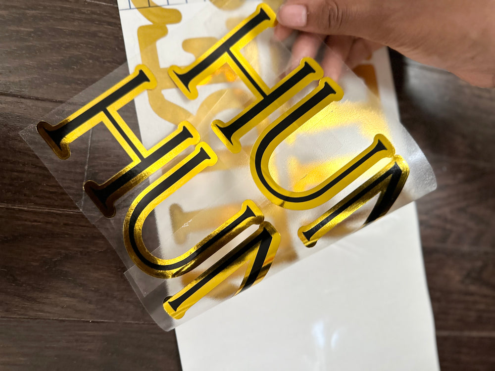 Hand lifting backing from gold and black layered lettering