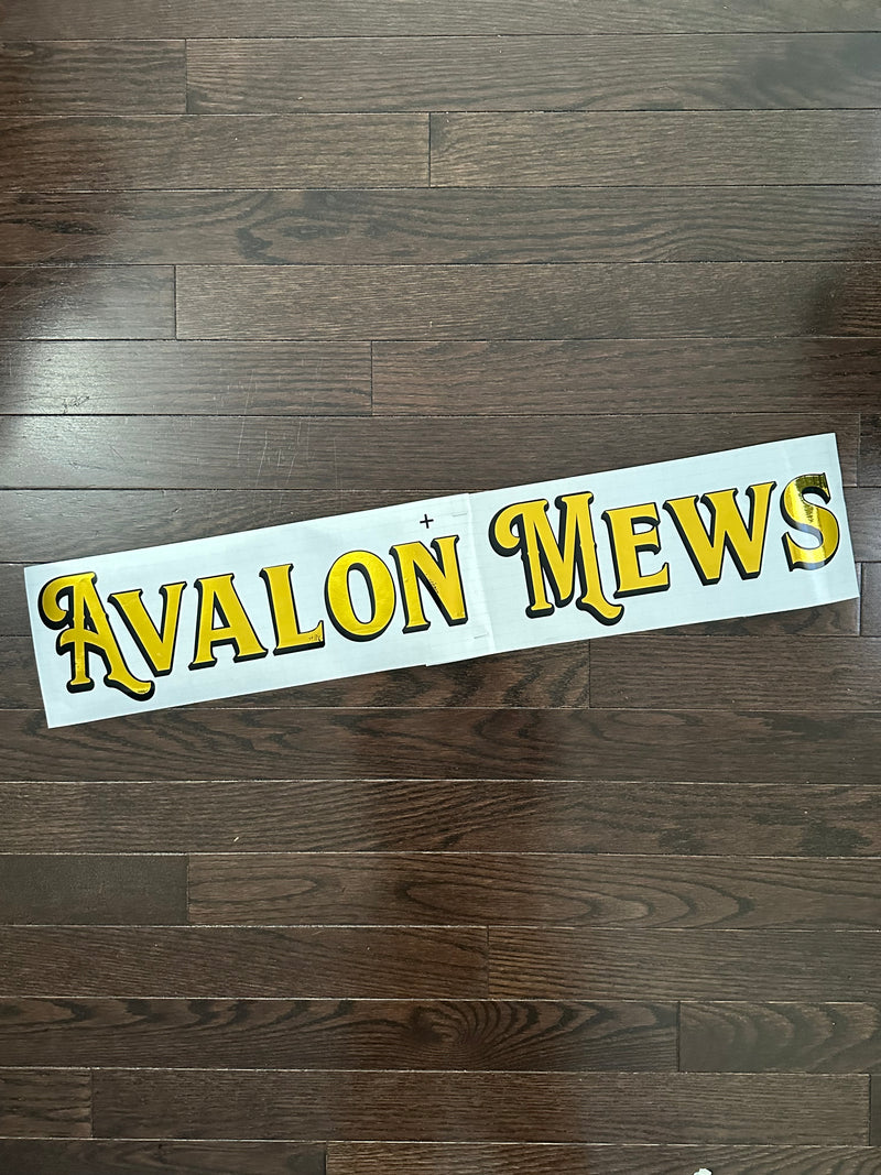 Gold and black Avalon Mews lettering on backing