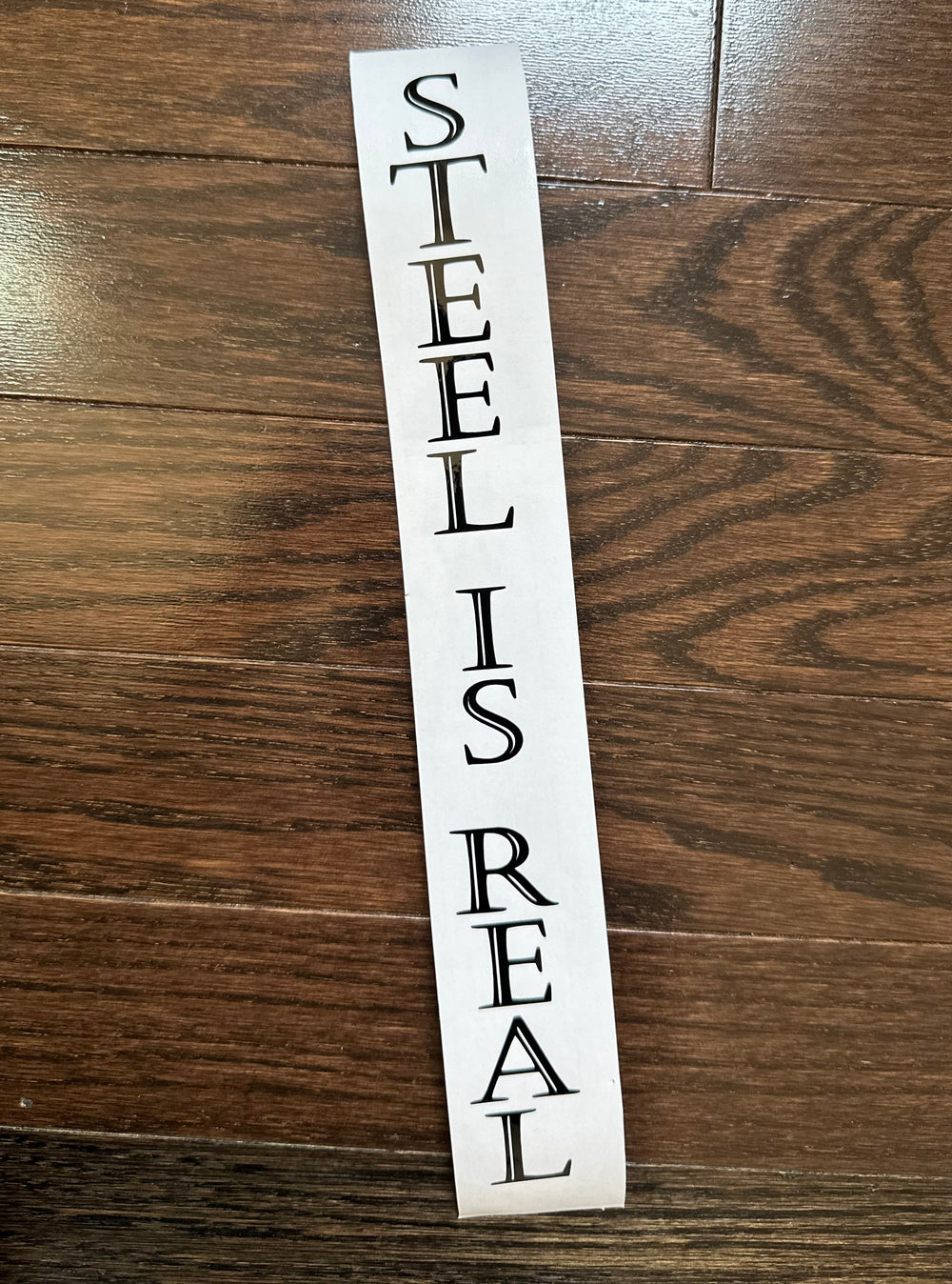 Black STEEL IS REAL lettering stacked vertically