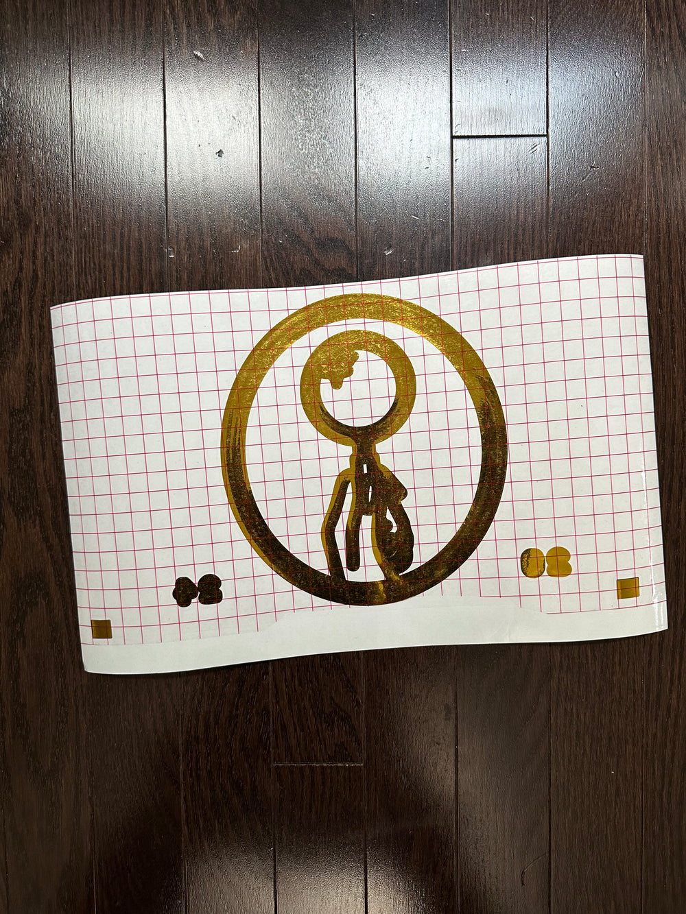 Gold and black circular logo on gridded transfer tape