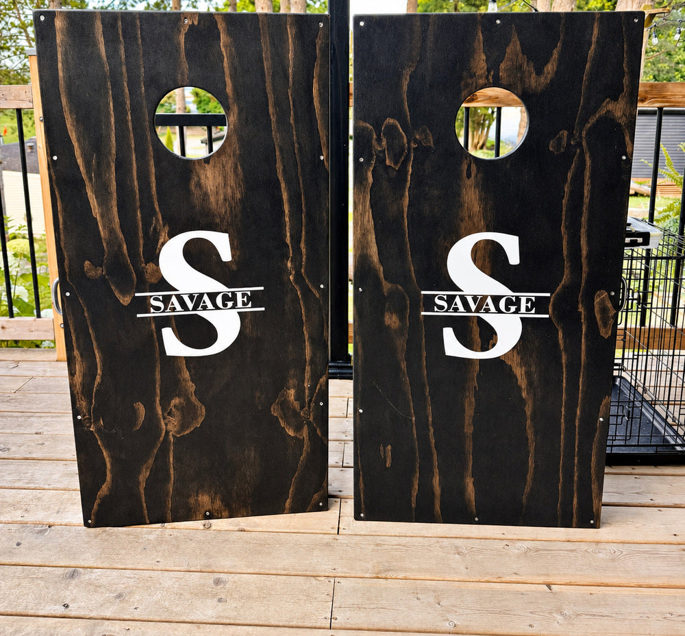 Two dark cornhole boards with white Savage split monograms