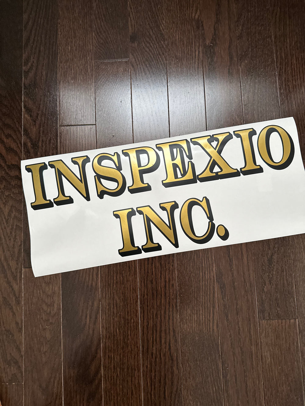 Gold and black Inspexio Inc. lettering on backing