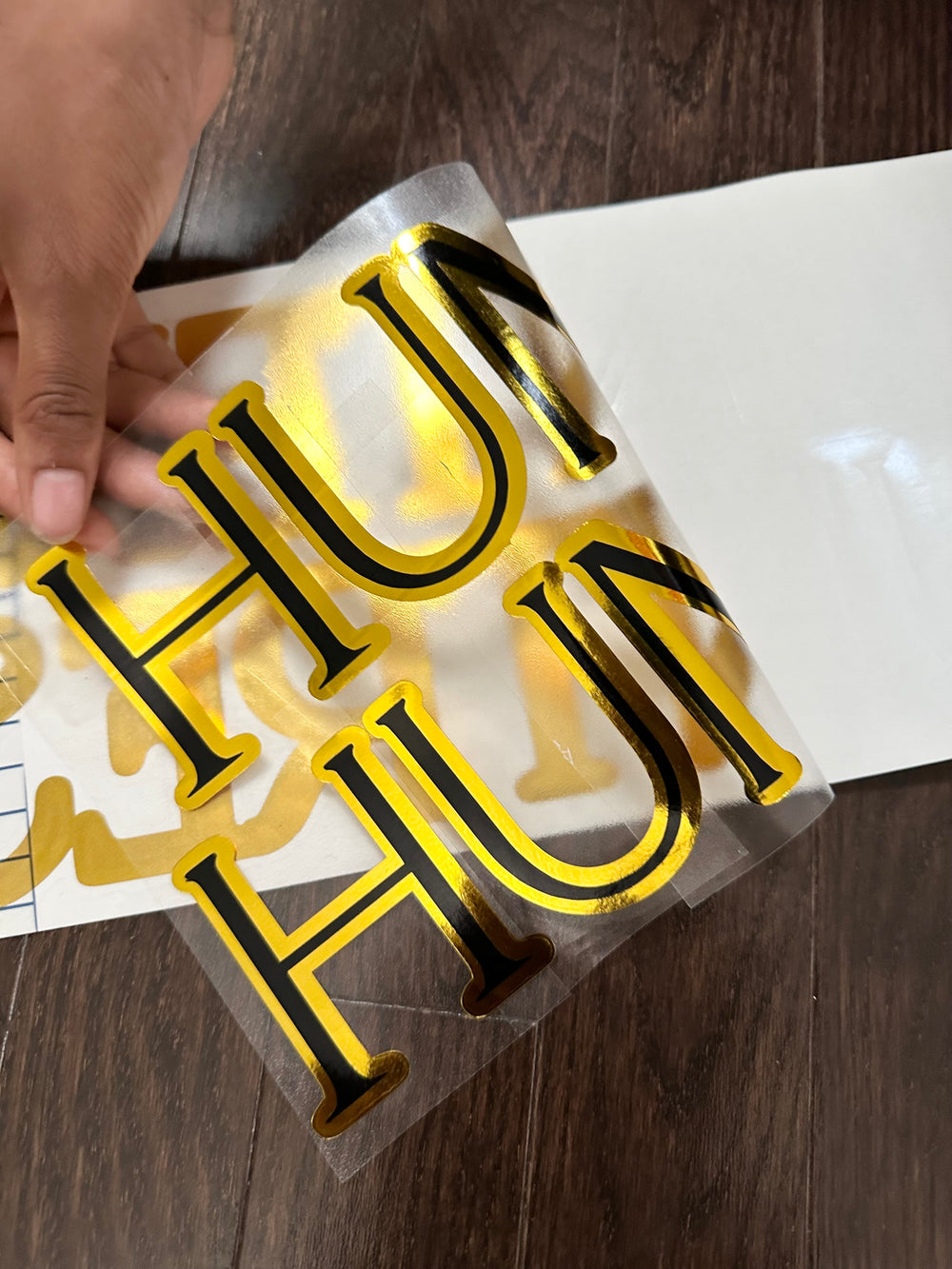 Gold and black layered lettering with backing being peeled