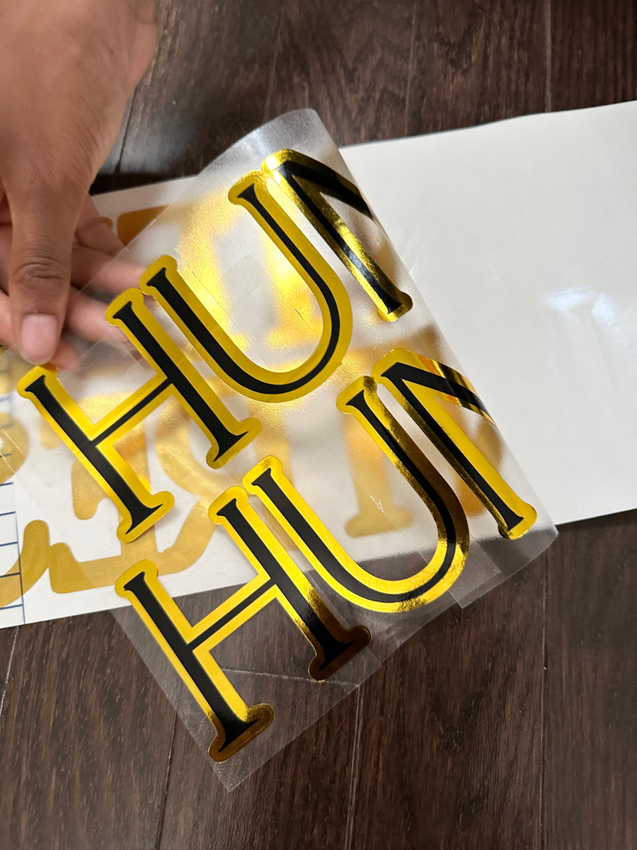 Gold and black layered lettering with backing being peeled
