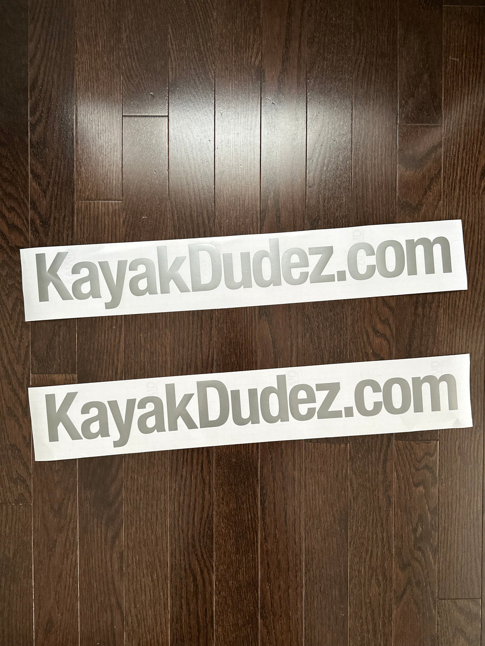 Two grey KayakDudez.com decals on backing