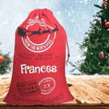 Red personalized Frances Santa sack beside a Christmas tree
